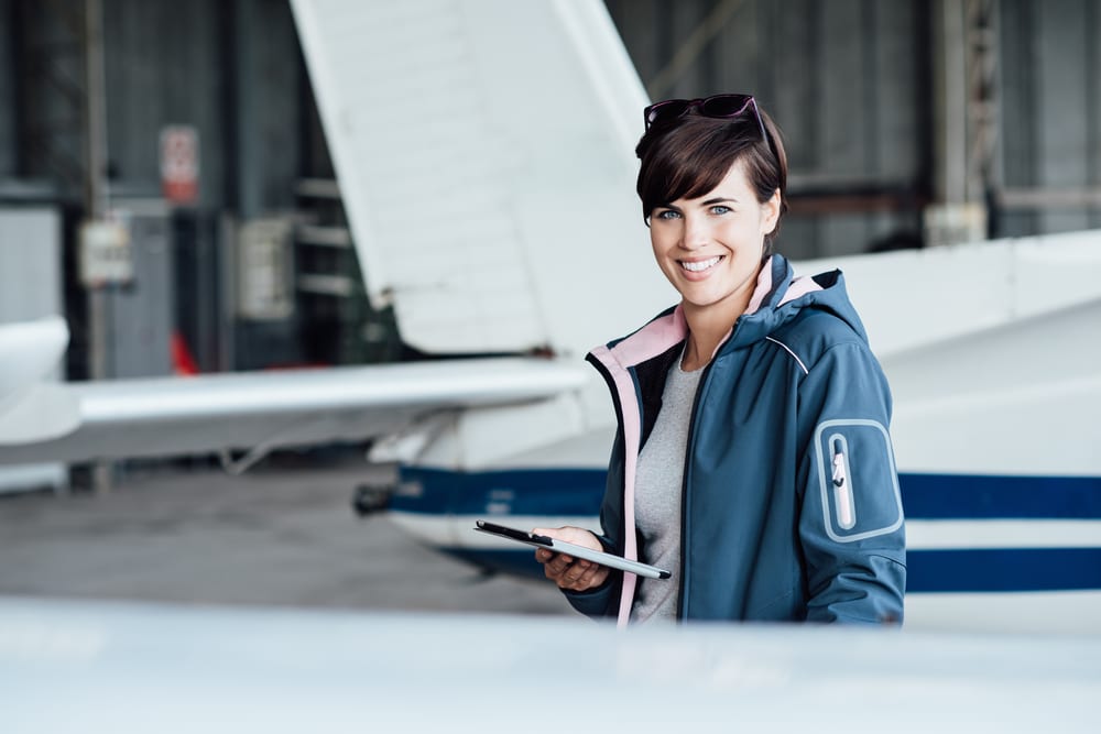 Smiling female pilot connecting with a digital tablet and using aviation apps